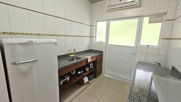 Uma cozinha compacta com paredes revestidas de azulejos brancos, frigorífico embutido, pia e janela com persianas.