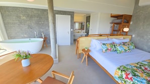 Un dormitorio moderno con una cama grande, una silla de madera, una mesa redonda con una planta y una bañera.