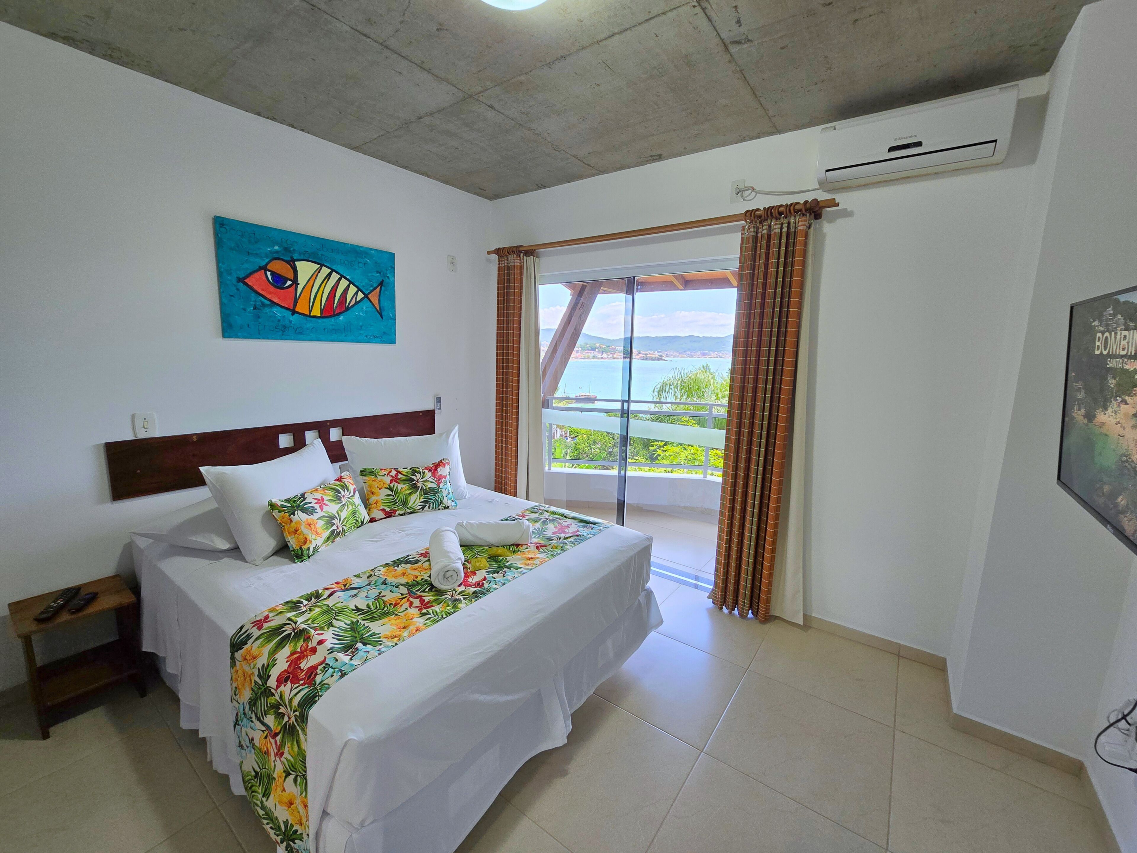 Une chambre d’hôtel avec un lit, une table de chevet, un tableau, un appareil de climatisation et une vue sur la mer.