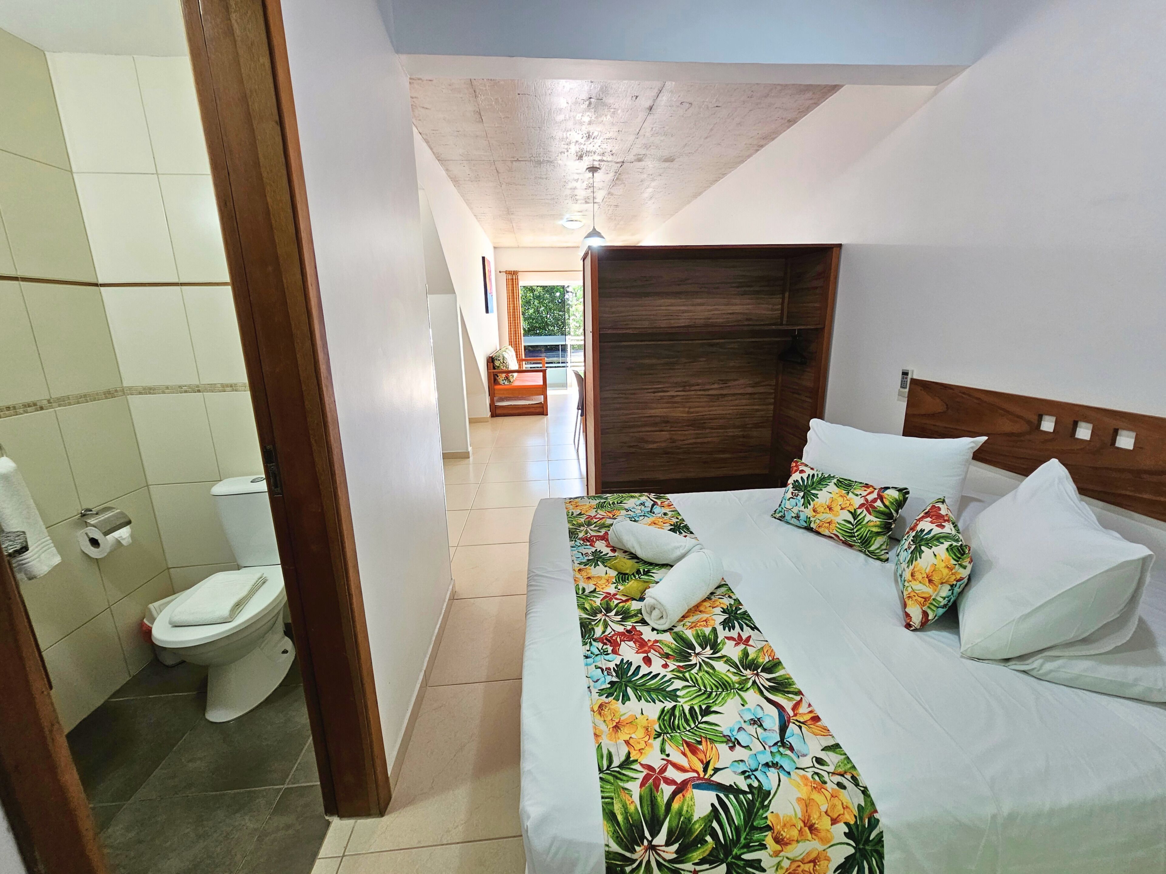 A hotel room with a bed, a wooden headboard, a toilet, and a window with curtains.