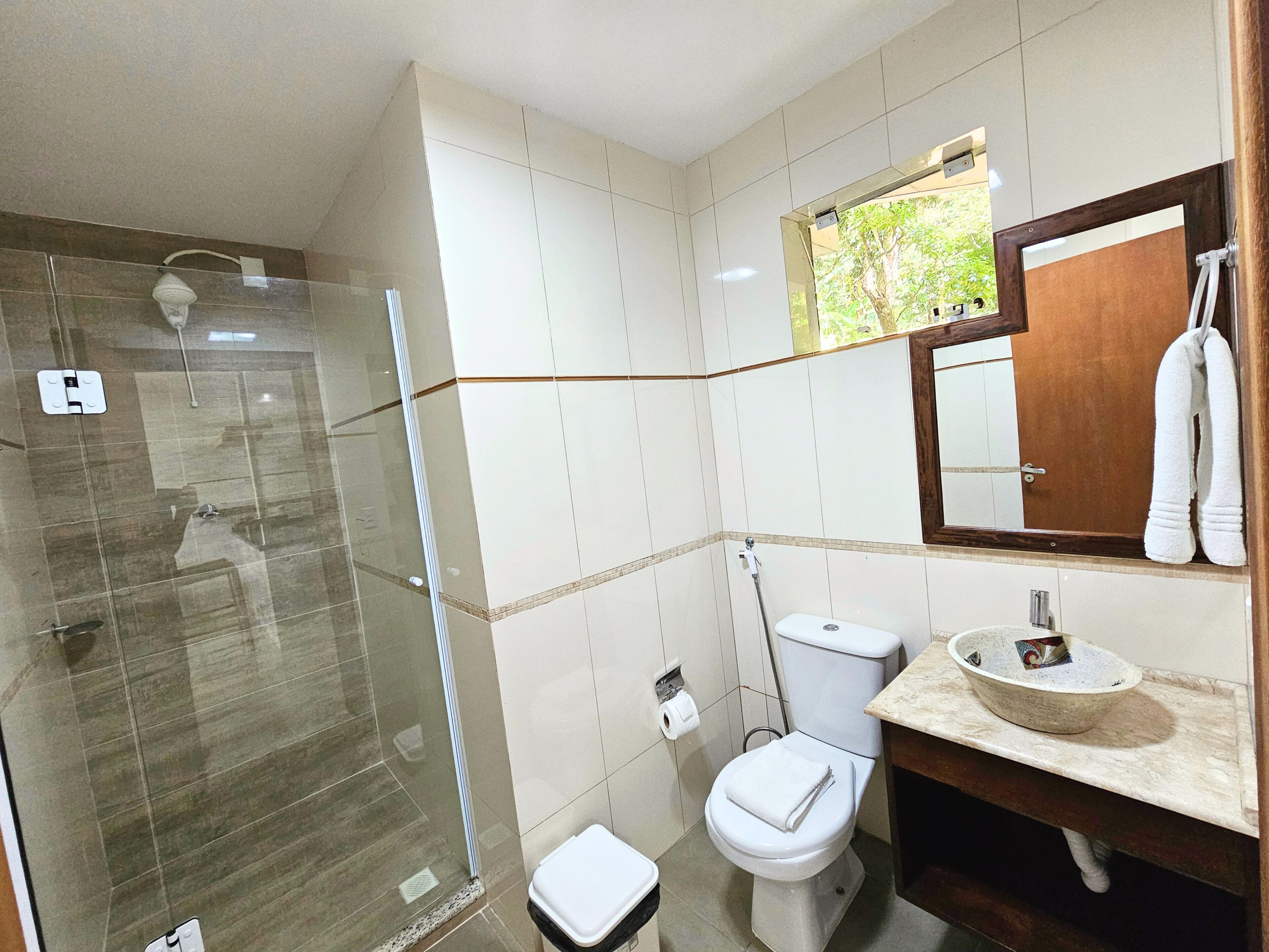 Un baño con cabina de ducha de vidrio, inodoro, lavabo y espejo sobre él.