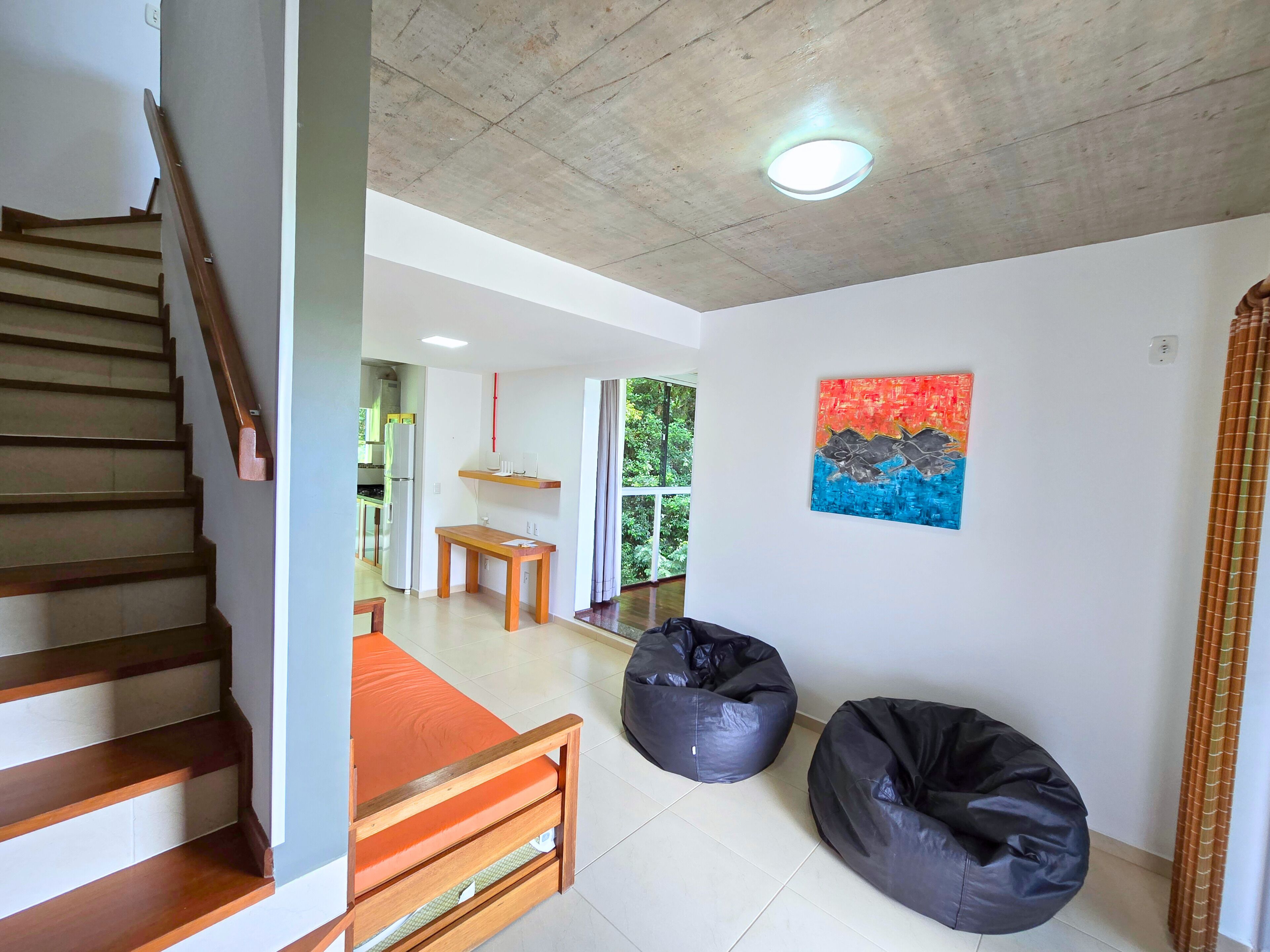 Un interior moderno con una escalera, una zona de comedor, sillones tipo bean bag y un cuadro en la pared.
