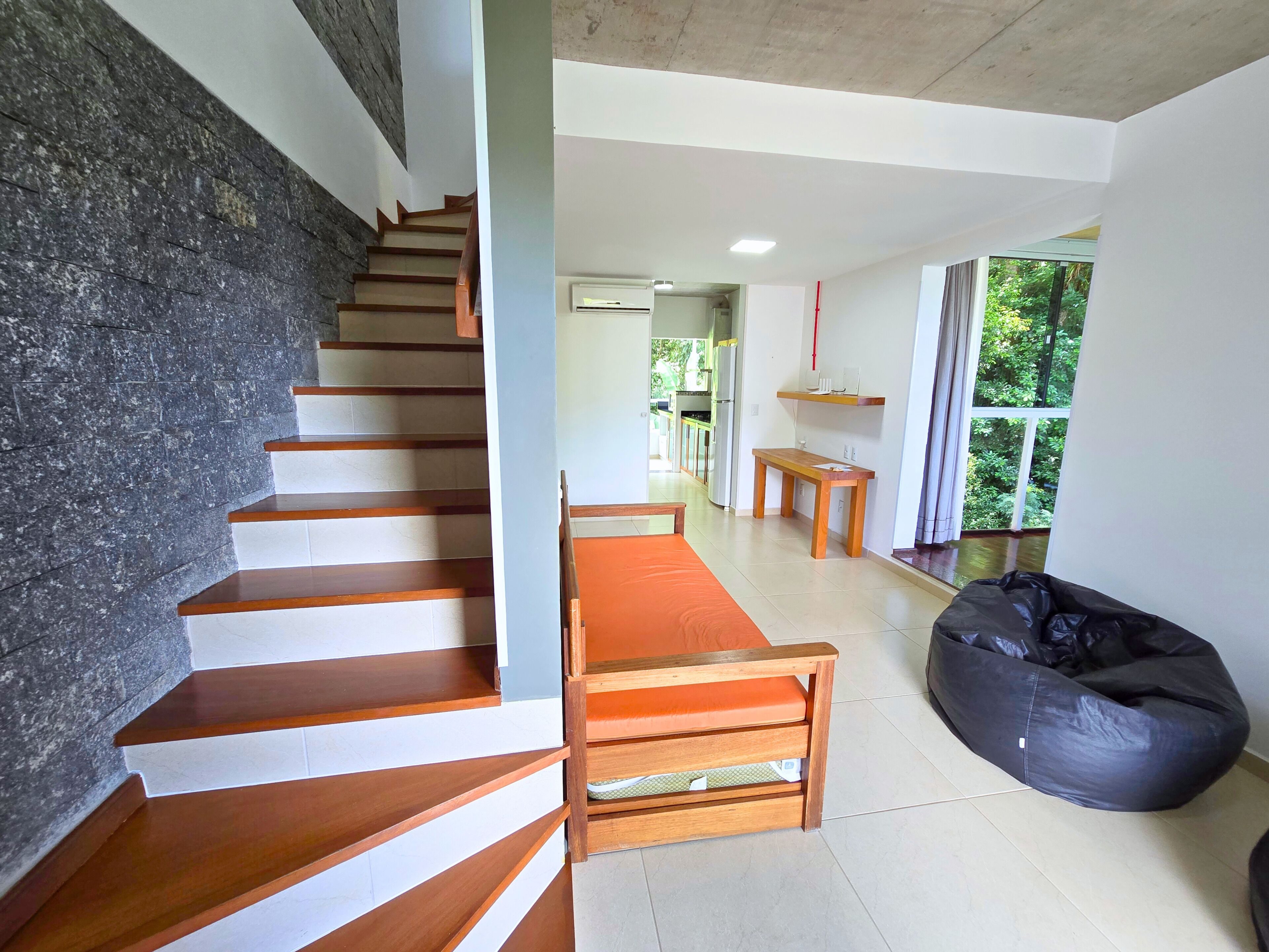 Un interior moderno con una escalera, un sillón de peluche y vistas al exterior.