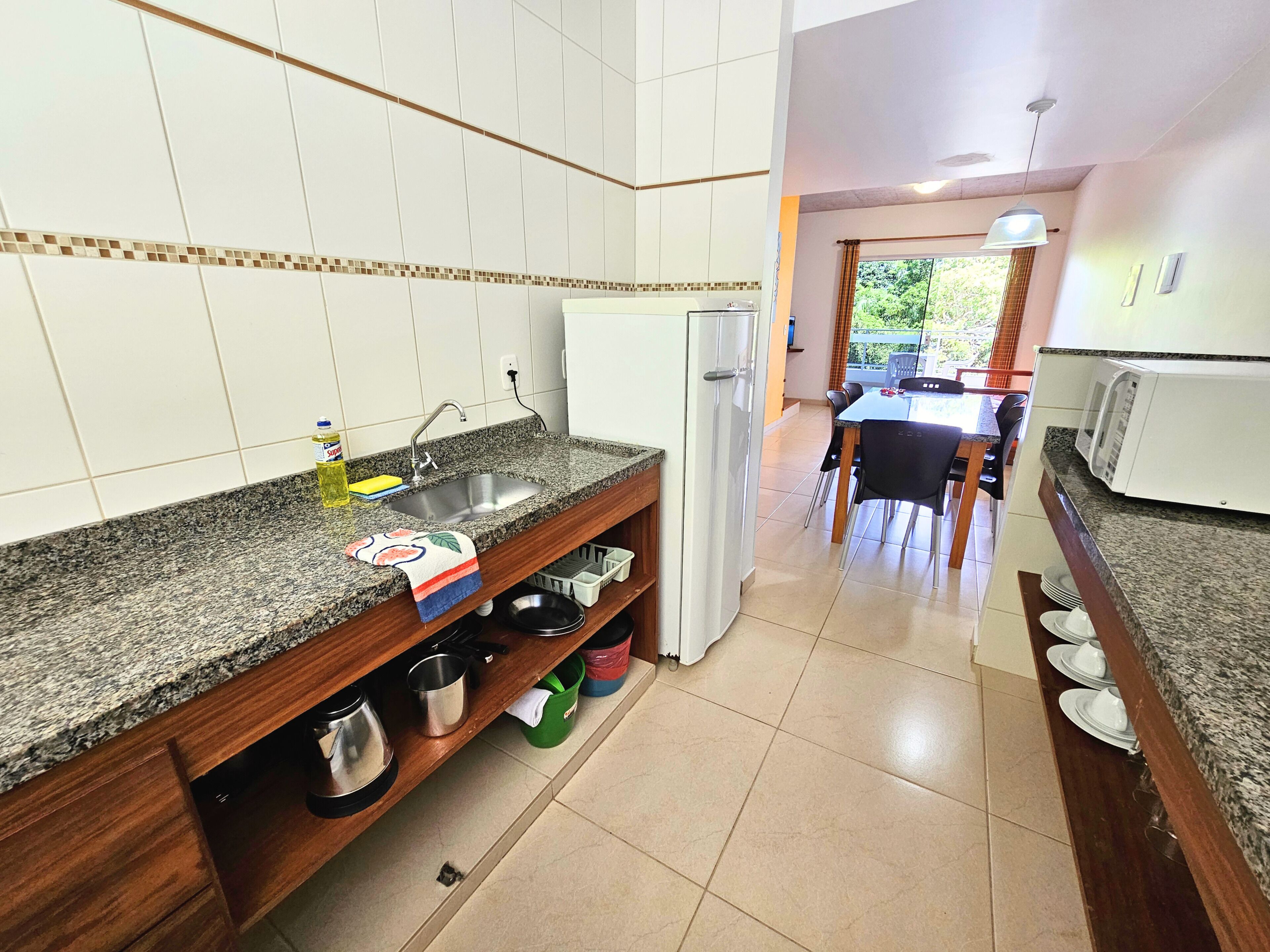 A kitchen with granite countertops, a stainless steel sink, and a refrigerator. There is a dining area with a table and chairs visible in the background.