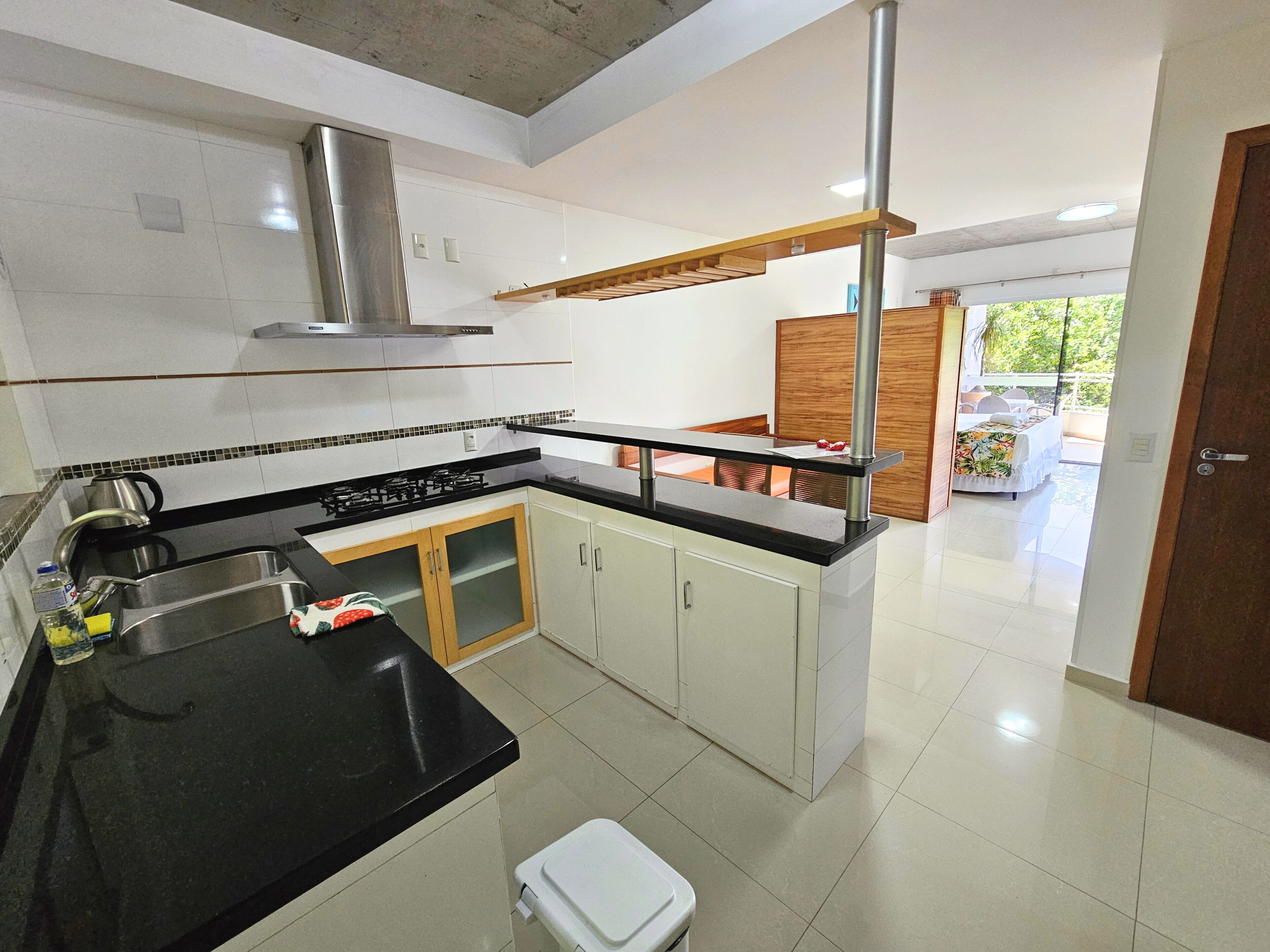 A modern kitchen with a black countertop, stainless steel appliances, and a wooden dining area.
