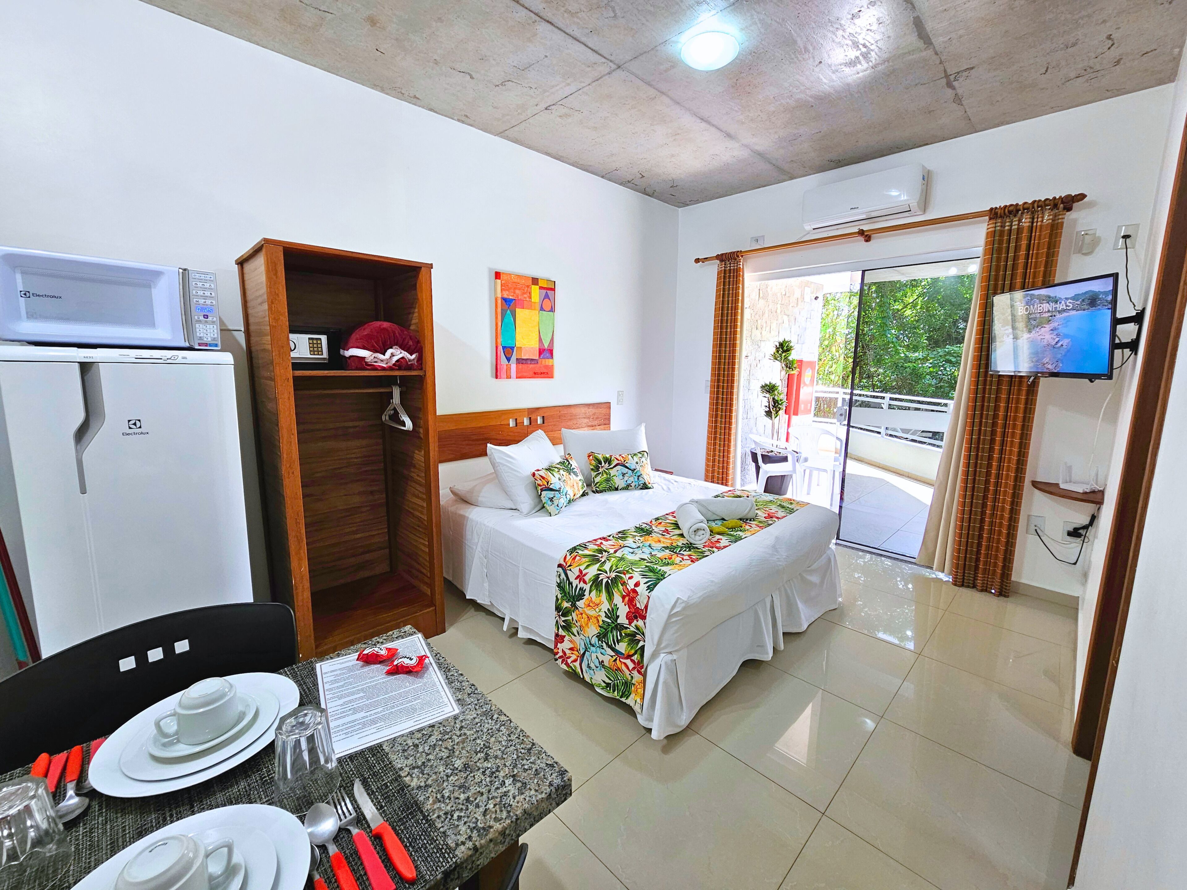 A hotel room with a bed, a dining table with cutlery, a microwave, and a TV.