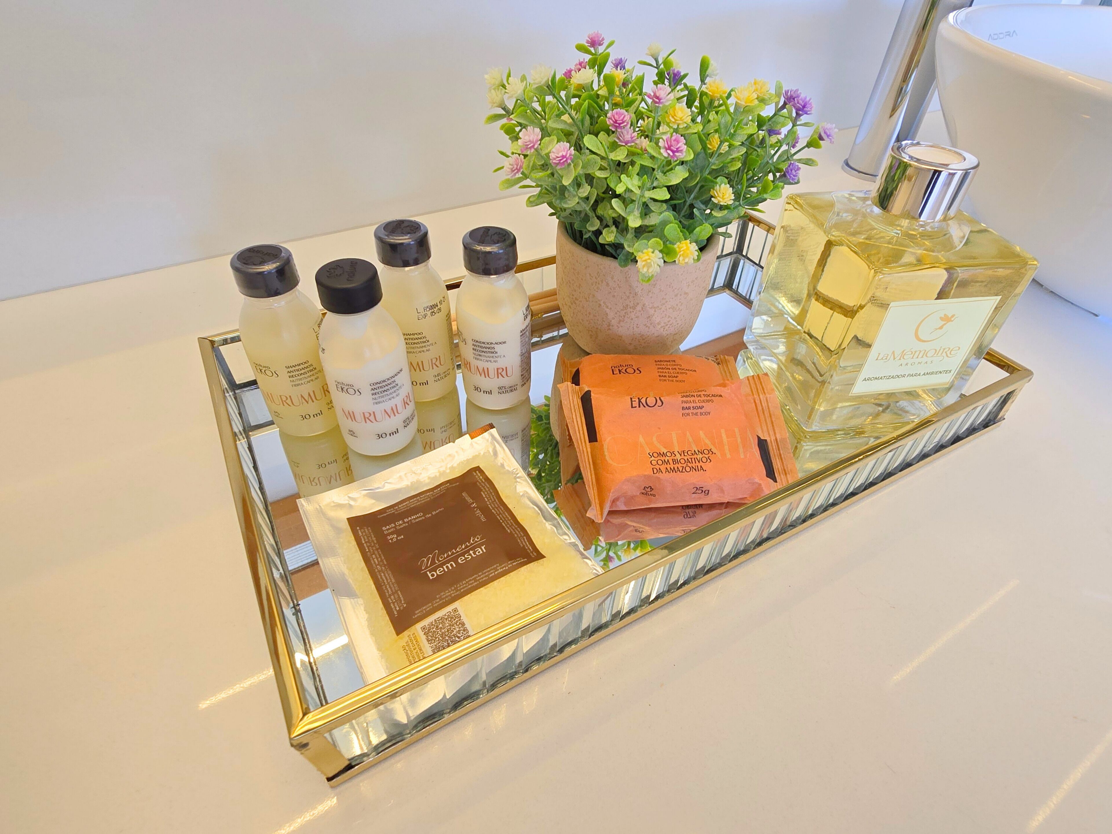 Een dienblad met diverse toiletartikelen, waaronder flessen shampoo, conditioner en douchegel, een potplant, een parfumfles en een pak zeep.