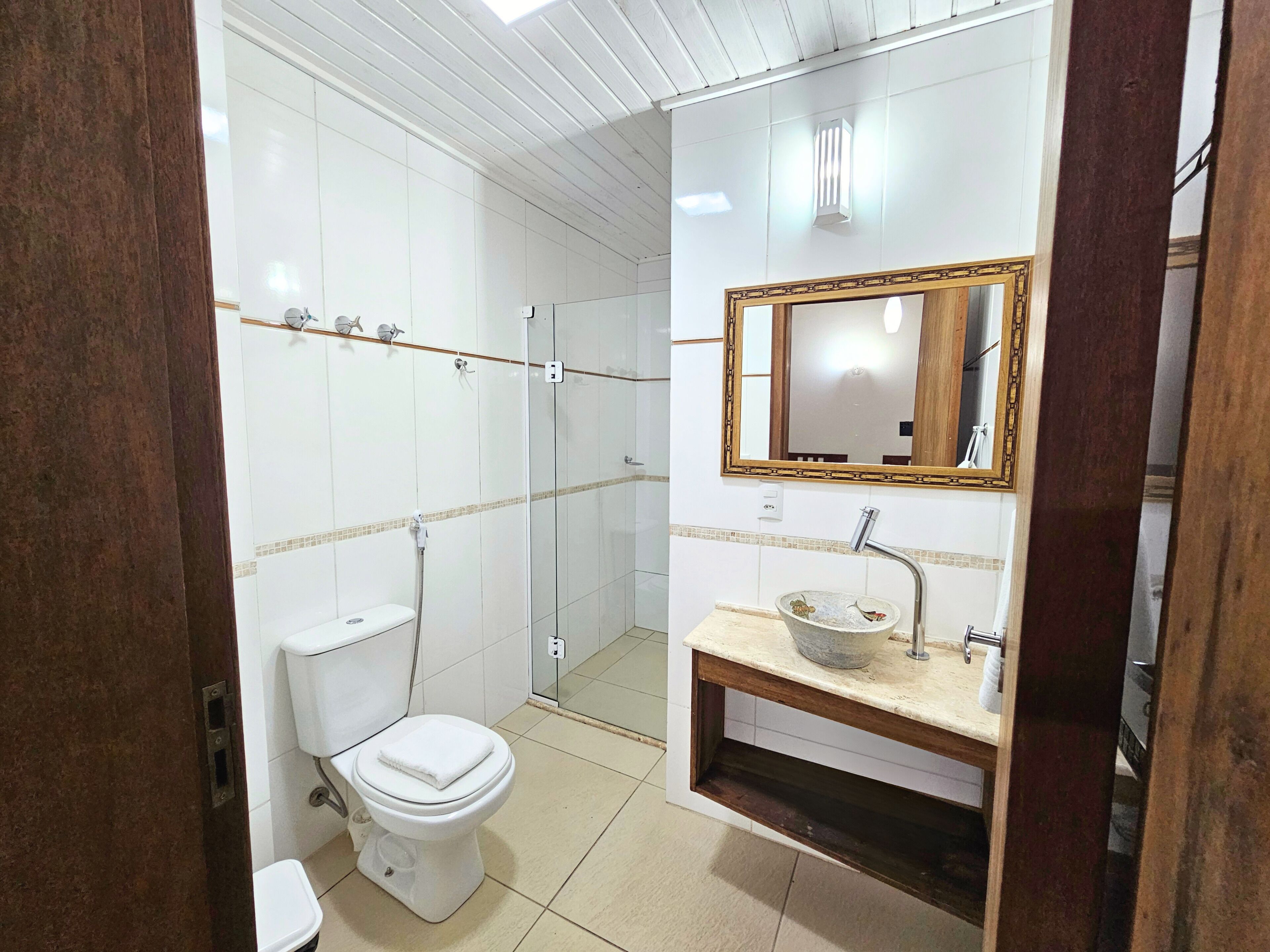 A bathroom with a toilet, a sink with a decorative basin, a shower area, and a mirror with a wooden frame.