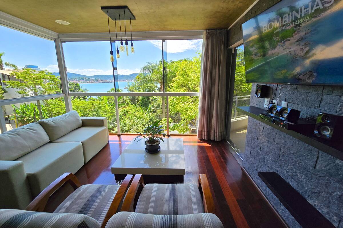 Uma sala de estar moderna com uma janela grande, um sofá, uma mesa de centro e uma TV na parede.