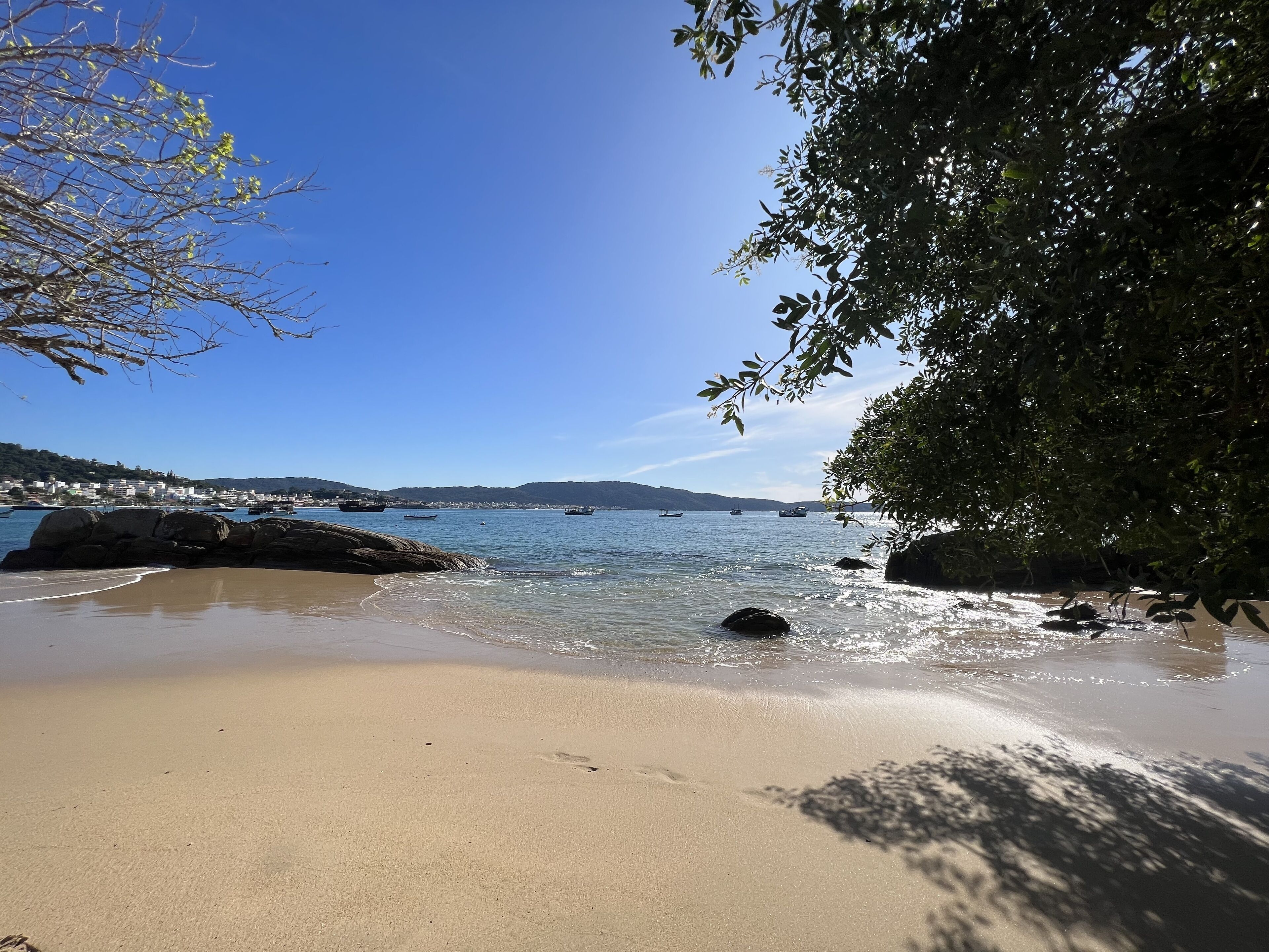 A beach with clear water, rocks, and a distant town.