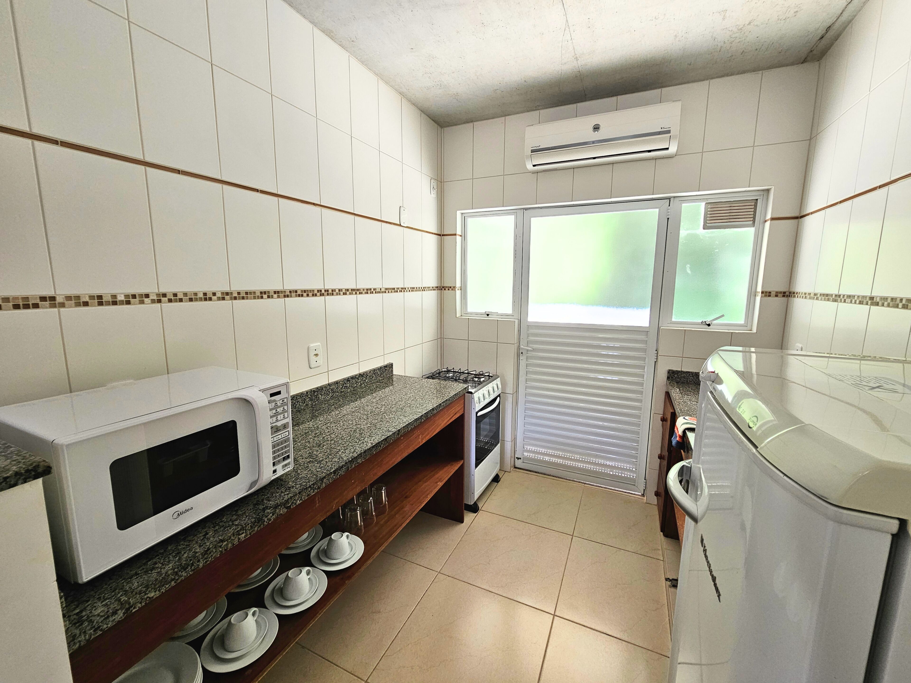 A compact kitchen with white tiled walls, a microwave, an oven, a gas stove, and a refrigerator.