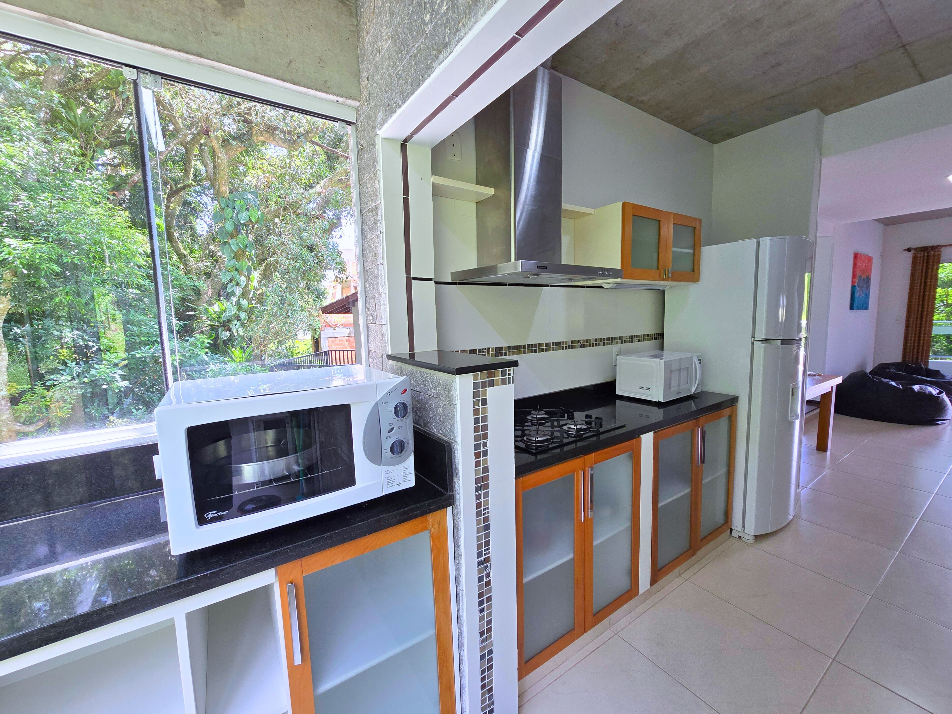 Cocina equipada con microondas, estufa y refrigerador. Se ve vegetación a través de la ventana.