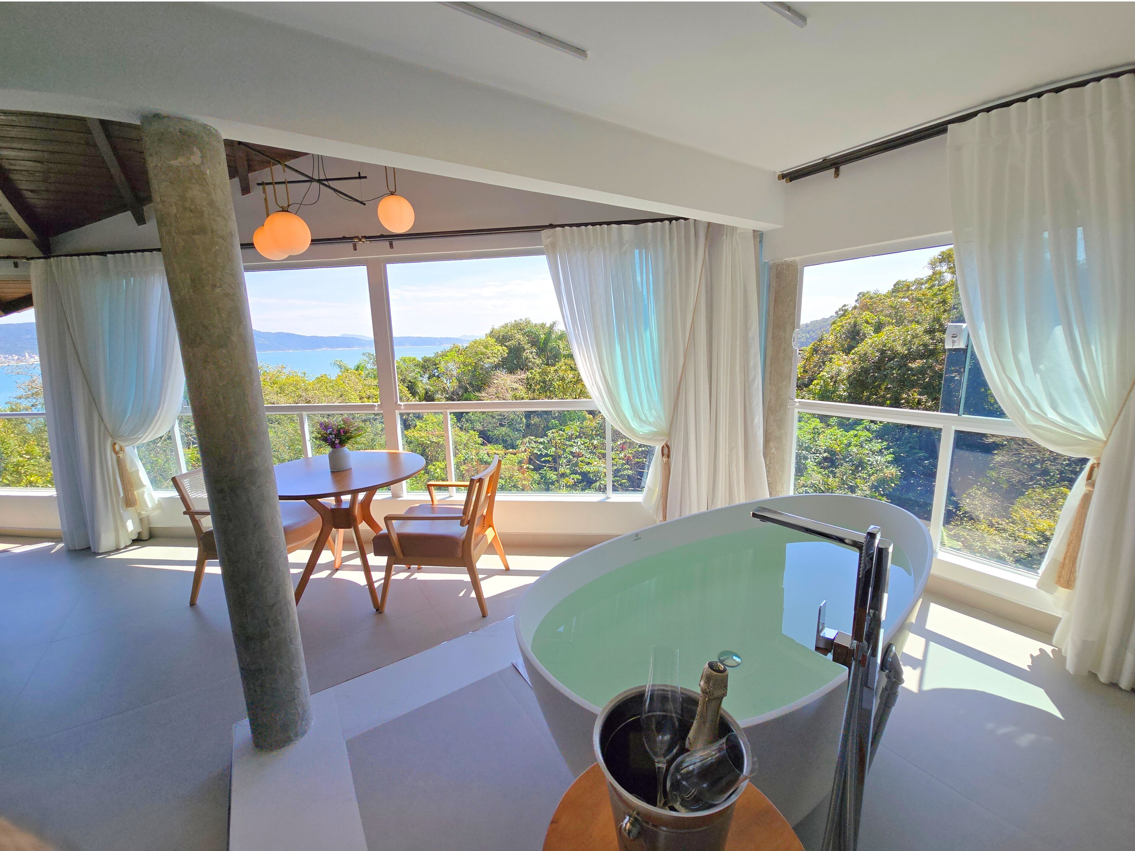 A modern room with a large bathtub, a dining table with chairs, and a view of the outdoors.