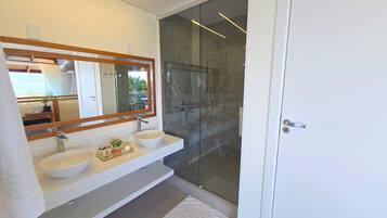 Un baño moderno con un espejo grande, dos lavamanos y una ducha con cerramiento de vidrio.