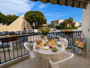 A balcony with a table set for breakfast, a chair, and a view of parked cars and buildings. - Sol-y-Days Hespérides, Family apartment 50m from the beach (Le Grau-du-Roi)