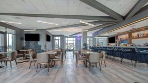 Un restaurante moderno con zona de bar, disposición de mesas y una amplia pantalla de televisión.