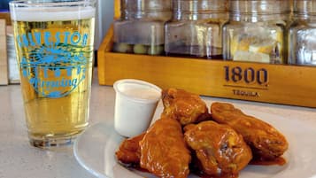 A glass of beer with a logo, a plate with wings, and a jar of sauce.