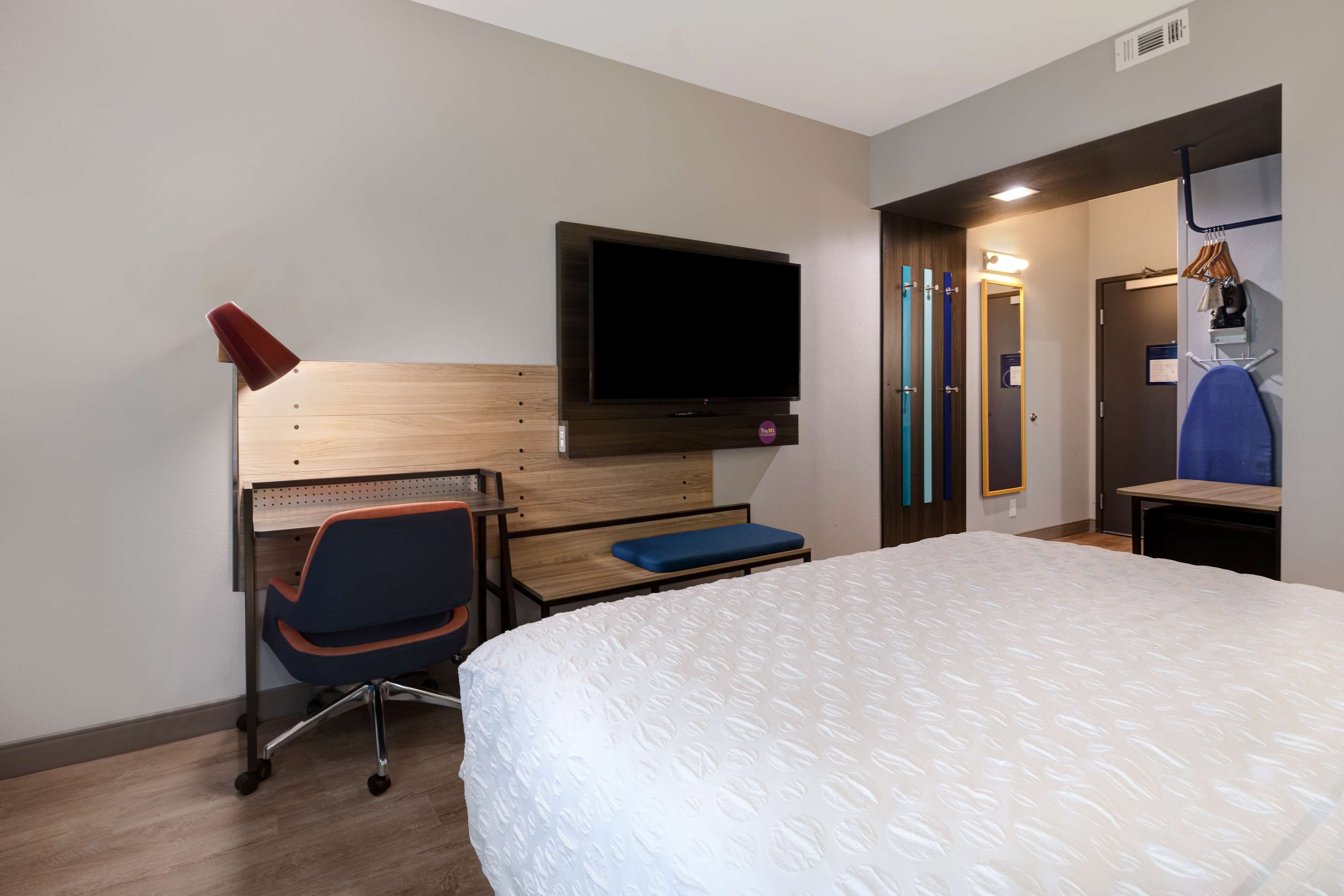 Ein Hotelzimmer mit Bett, Schreibtisch mit Stuhl, Wandfernseher und Tür zu einem Badezimmer.