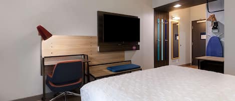 Ein Hotelzimmer mit Bett, Schreibtisch mit Stuhl, Wandfernseher und Tür zu einem Badezimmer.