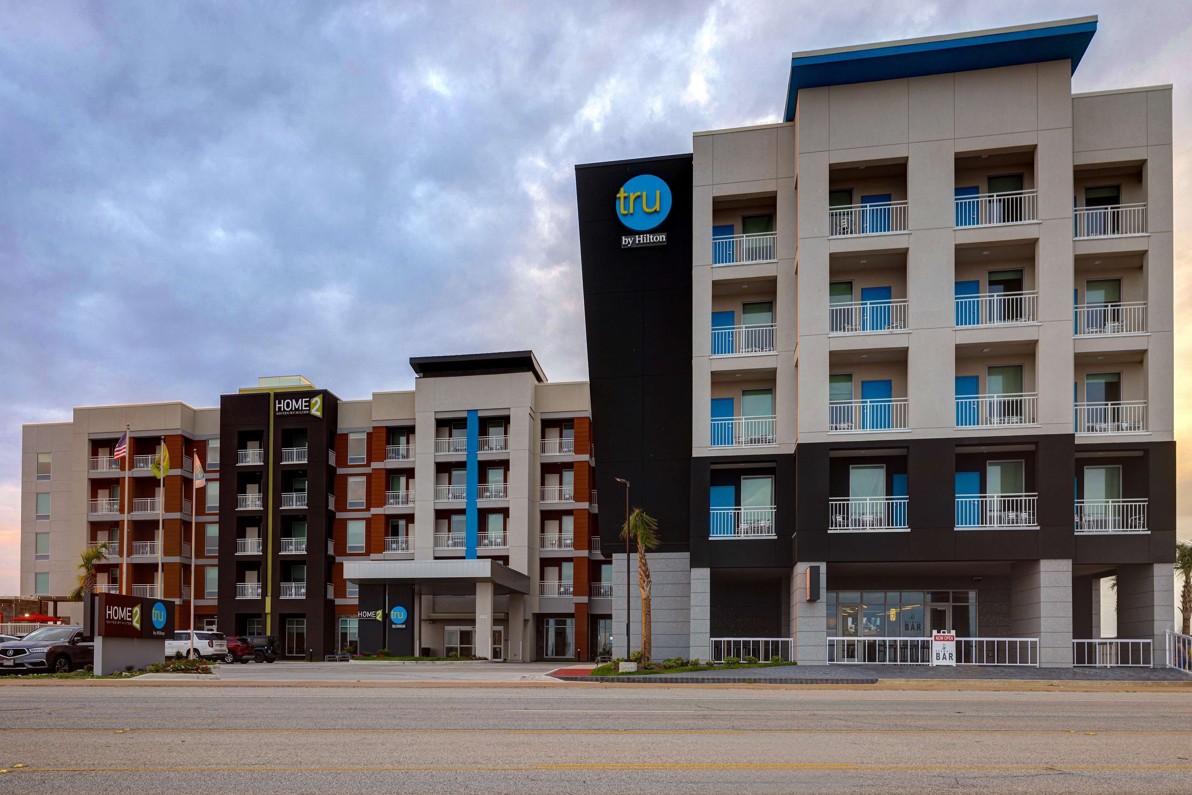 A multi-story hotel with a prominent 'tru by Hilton' sign, multiple balconies, and a parking lot in front.
