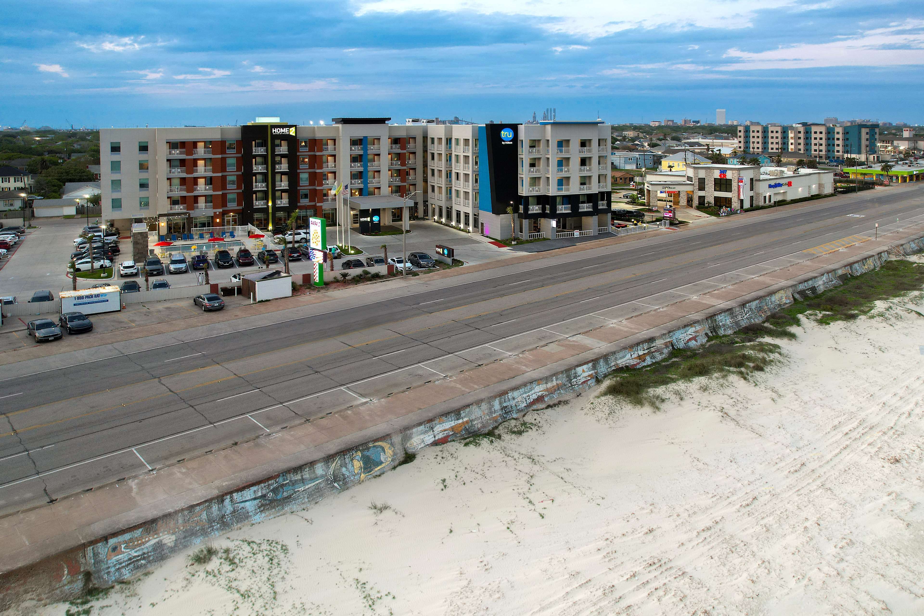 A hotel with multiple floors, a parking lot, and a beach view.