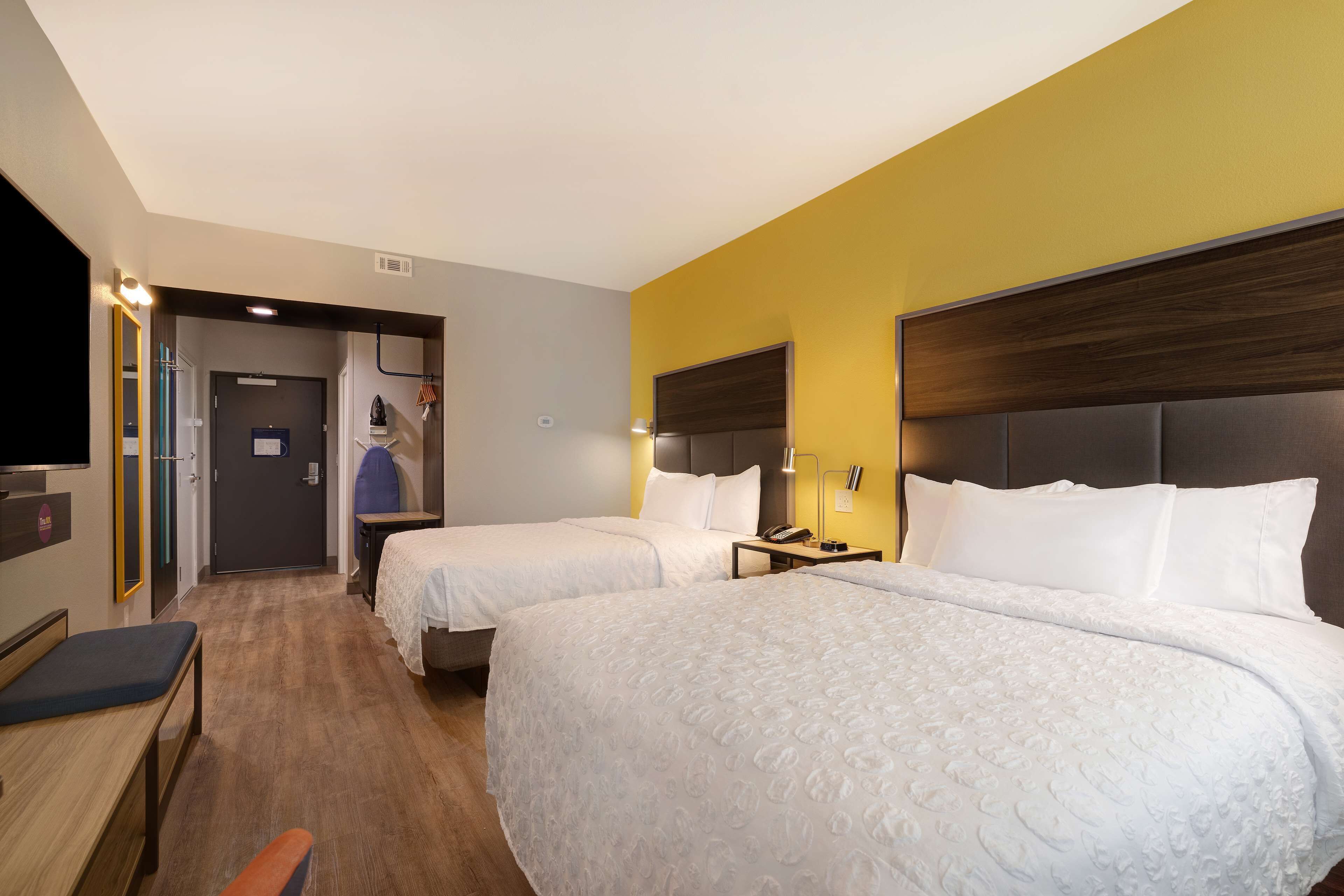 A hotel room with two beds, a desk, a chair, a TV, and a bathroom visible through an open door.