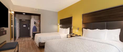 Une chambre d’hôtel avec deux lits, un bureau, une chaise, une télévision et une salle de bain visible à travers une porte ouverte.