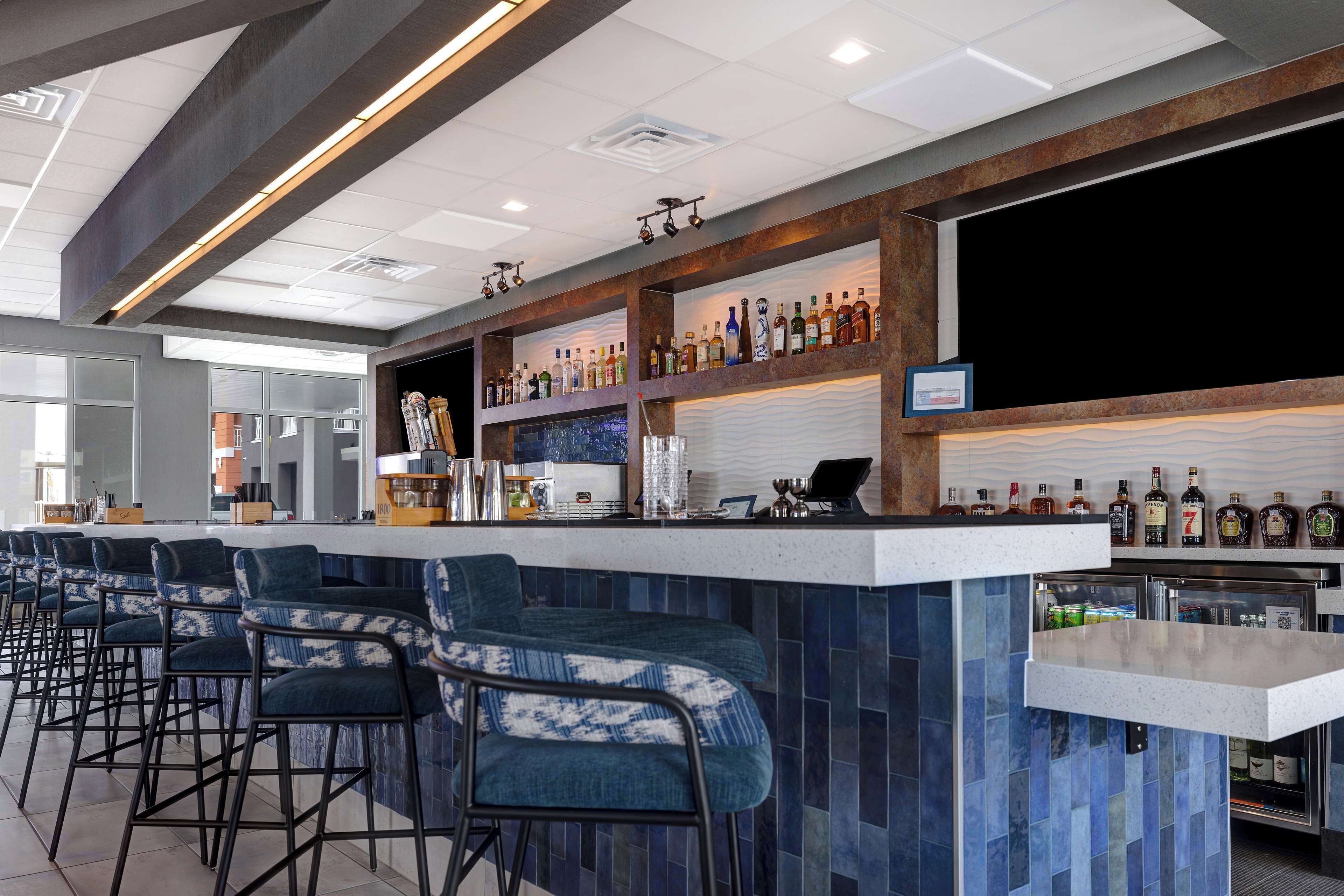 A bar area with a long counter, multiple stools, and shelves with bottles.