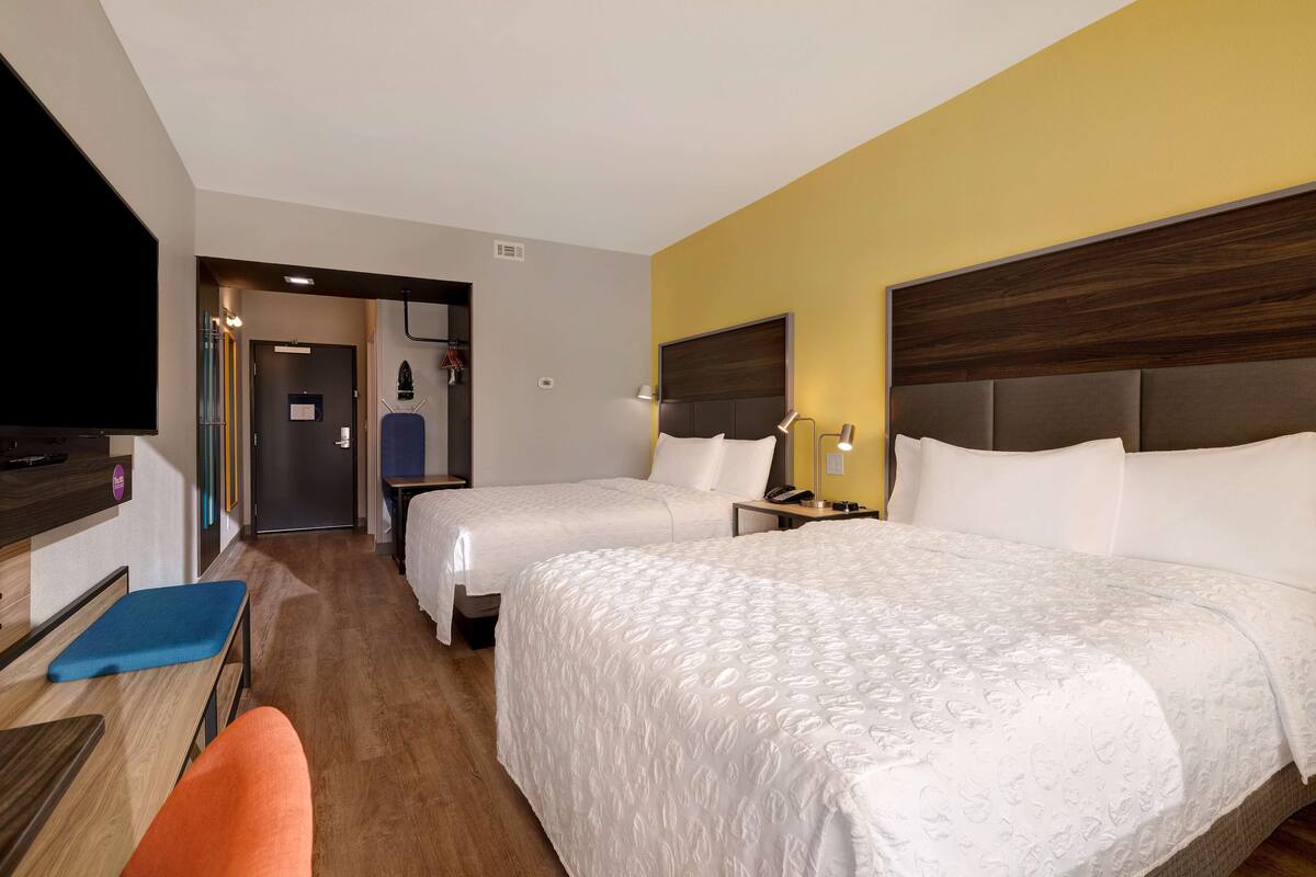 Een hotelkamer met twee bedden, een bureau, een stoel, een televisie en een deur naar een badkamer.