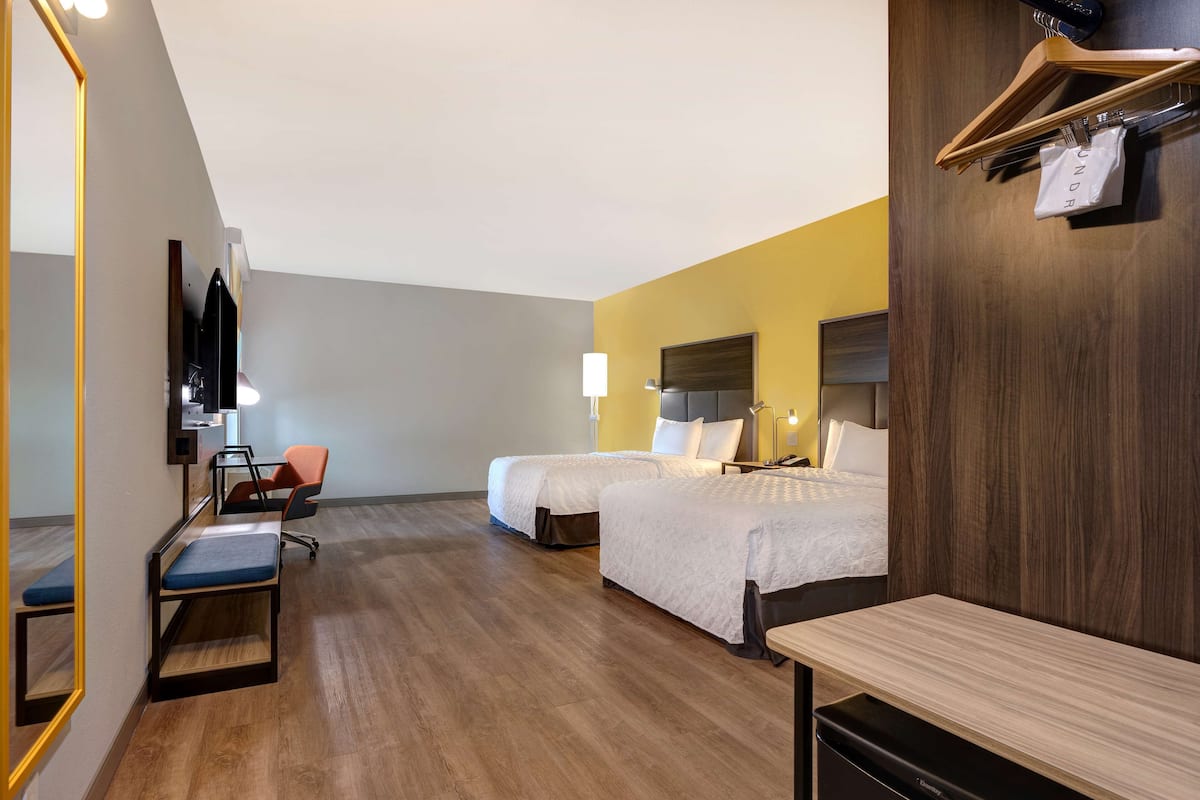 Een hotelkamer met twee bedden, een bureau, een stoel, een spiegel en een houten dressoir.