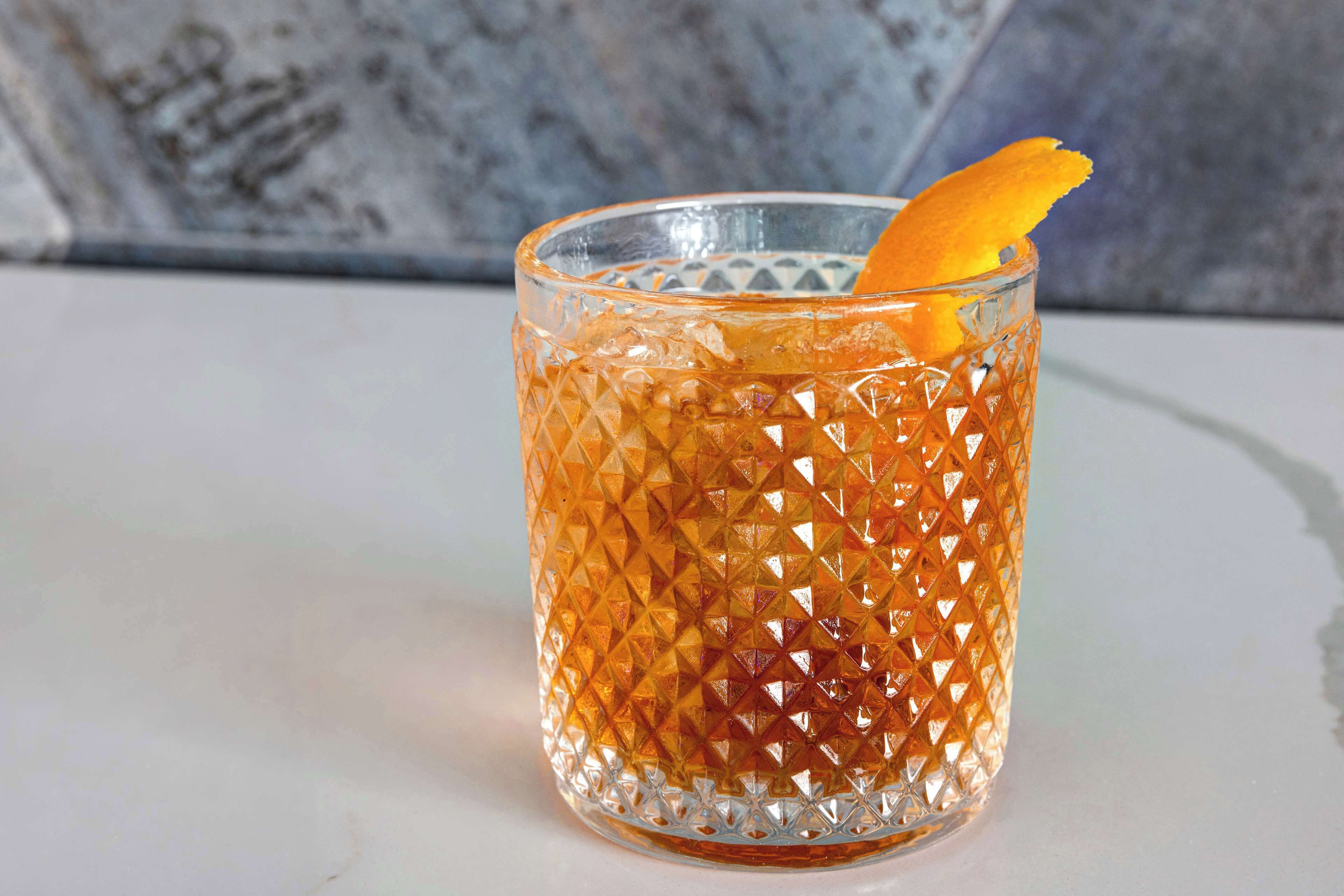 A clear glass with a textured pattern and an orange garnish.