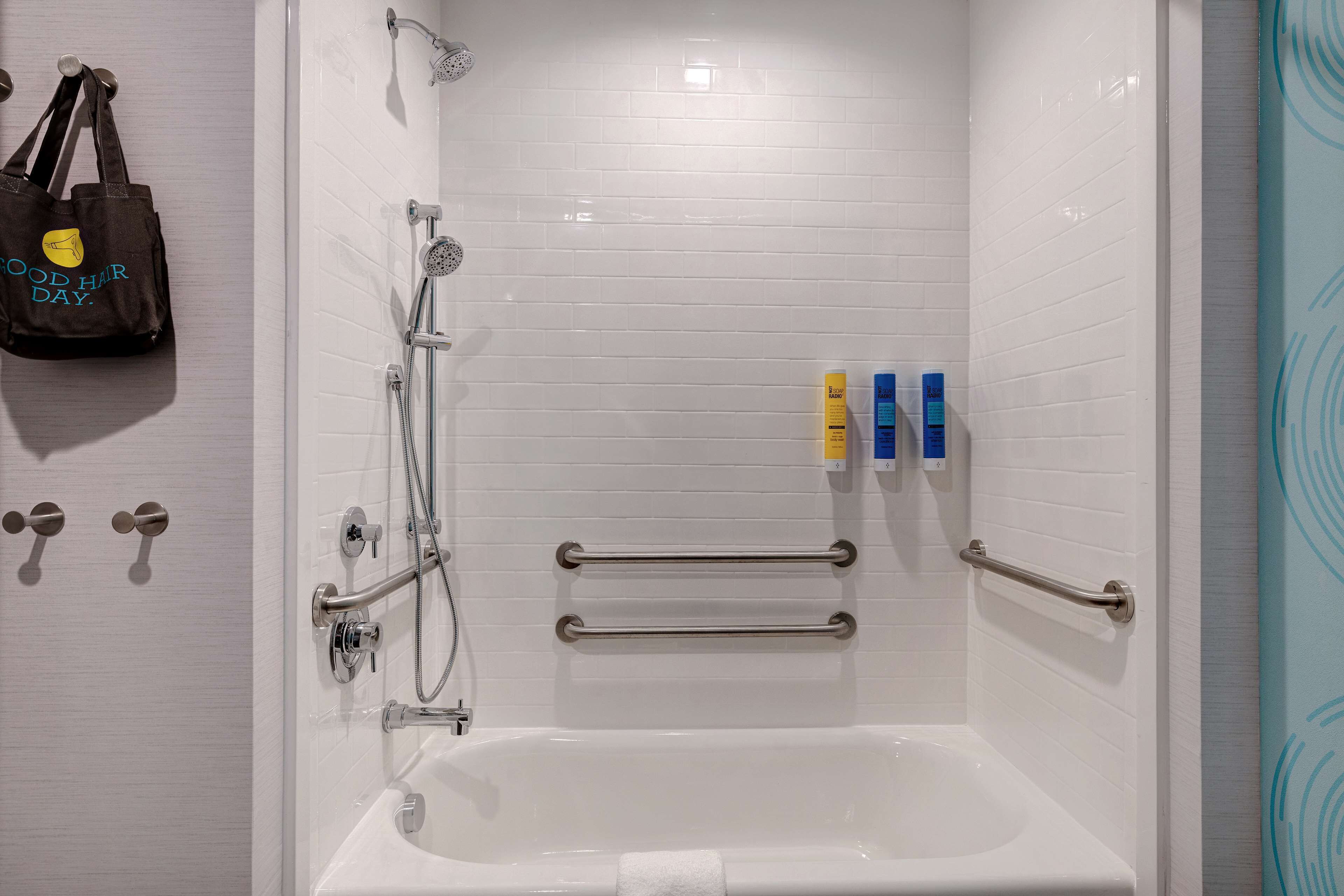 A bathroom with a white bathtub, grab bars, a towel rack, and a showerhead.