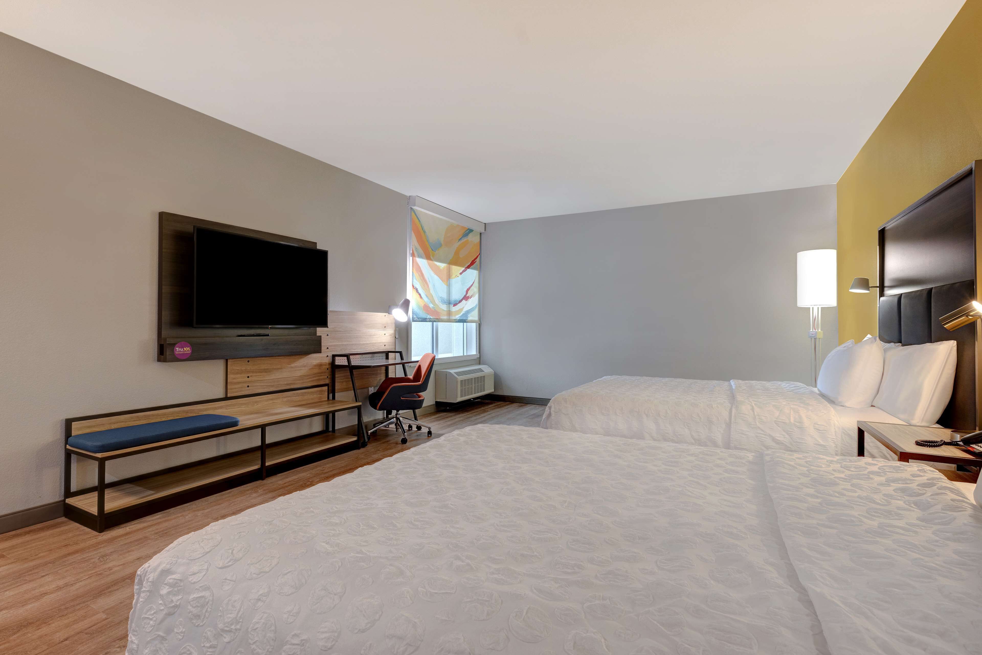 A hotel room with two beds, a desk, a chair, a TV, and a window with a view.