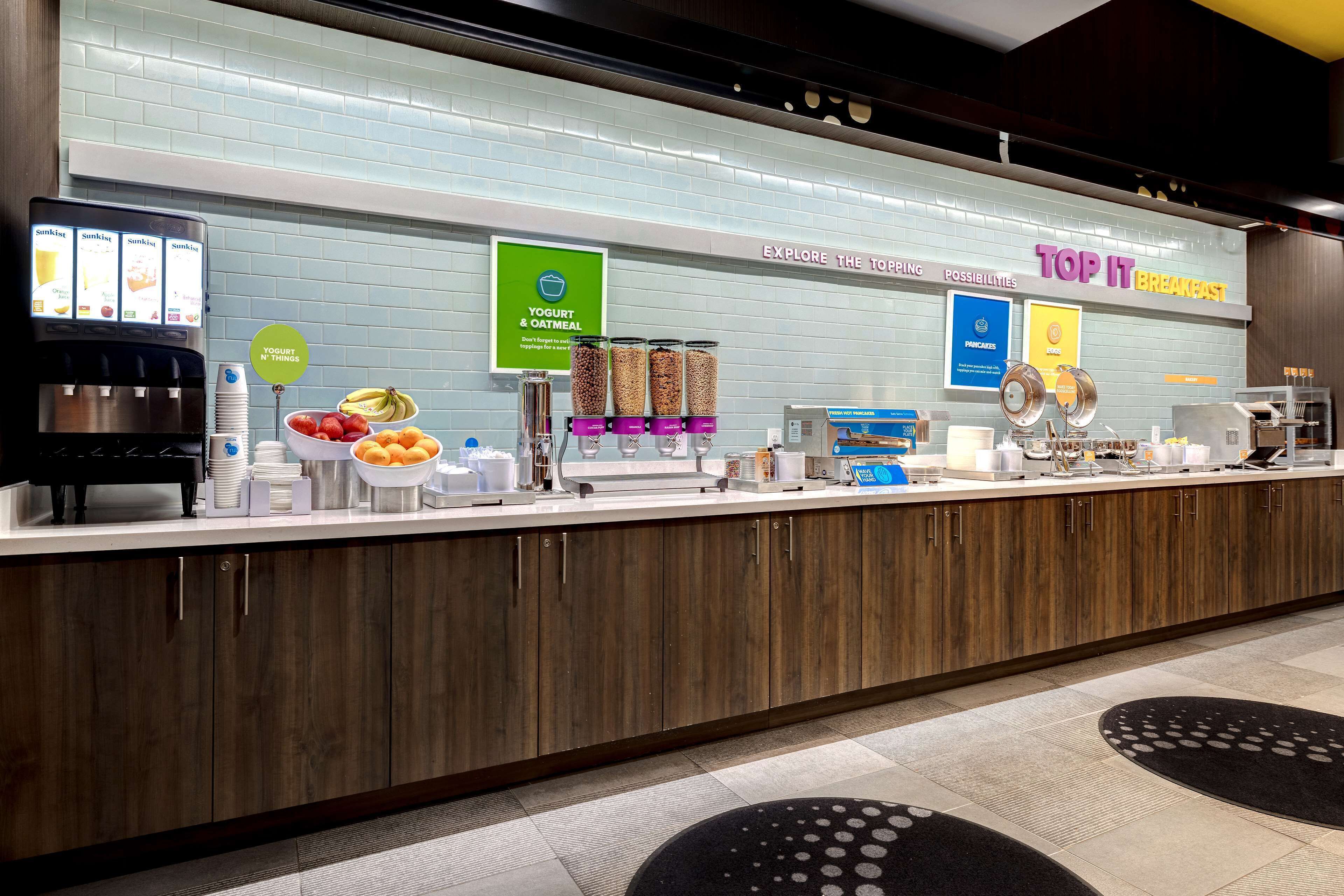 Un comptoir-buffet pour le petit-déjeuner avec des distributeurs de yaourt et de flocons d’avoine, une machine à café et un panneau indiquant « Top It Breakfast ».