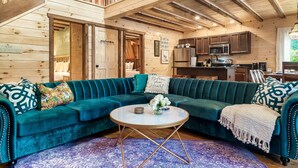 A cozy cabin interior with a teal sofa, wooden walls, a kitchen area, and a balcony. - Perfect for Girls Trips! 4 Suites & Amazing Pool! (Gatlinburg)