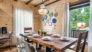 A wooden dining room with a table set for six, surrounded by chairs. There are plates and glasses on the table, and a chandelier hangs above. - Perfect for Girls Trips! 4 Suites & Amazing Pool! (Gatlinburg)