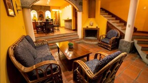 A cozy living area with wicker furniture, a fireplace, and a staircase leading to another room. - Beautiful Lakefront home: gardens  (Santiago Atitlan)