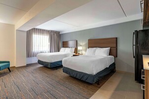Una habitación de hotel con dos camas, un escritorio, un refrigerador y una ventana con cortinas.