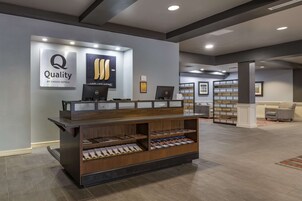 Un mostrador de recepción con detalles de madera, un letrero que dice "Quality by Choice Hotels" y un monitor de computadora.