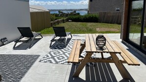 Un patio con dos sillones, una mesa de madera y vista al mar.