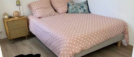 A bedroom with a bed, a nightstand, a lamp, a small rug, and a round ottoman.