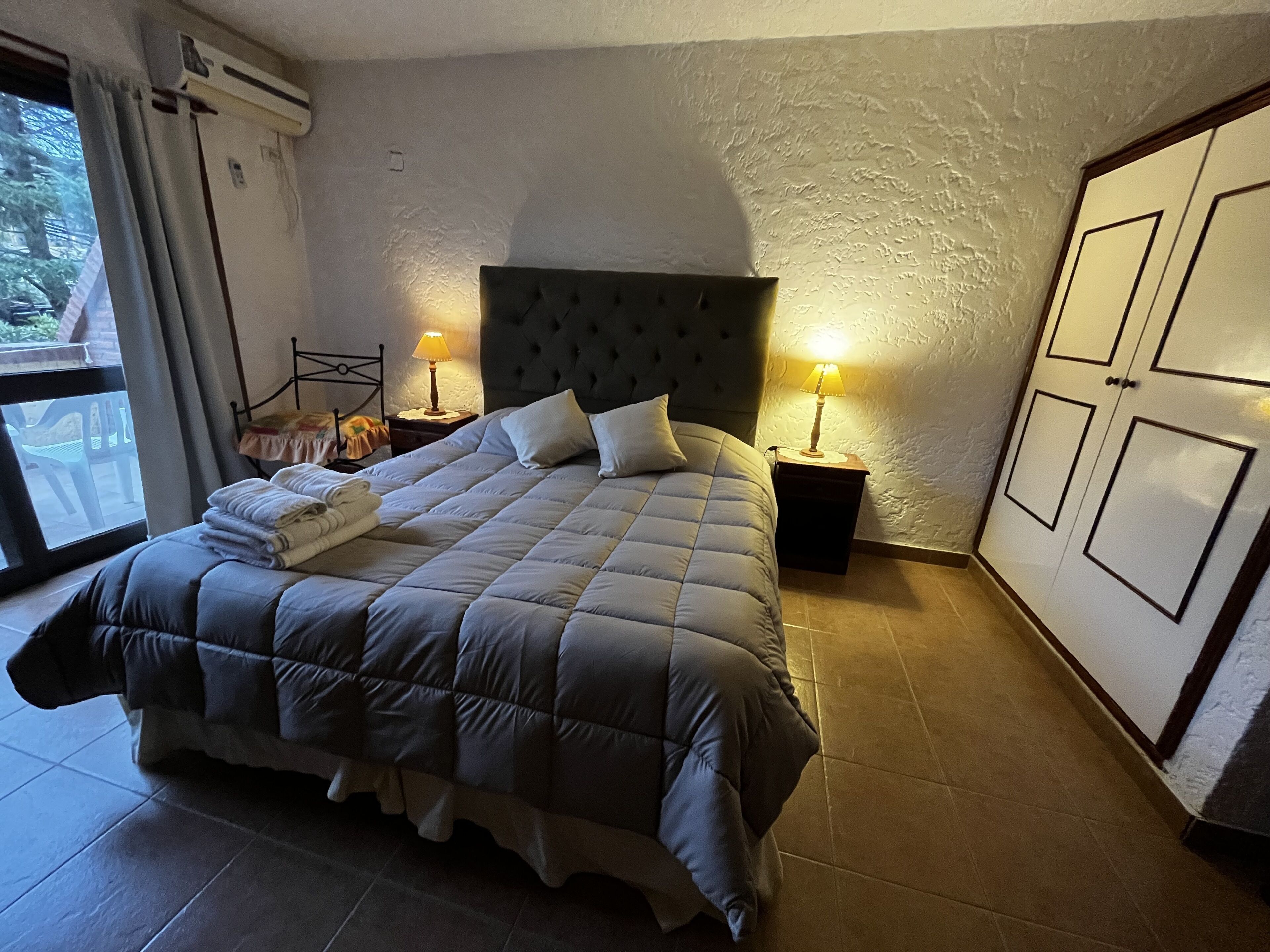 A bedroom with a large bed, two bedside tables with lamps, a wardrobe, and a window with curtains.