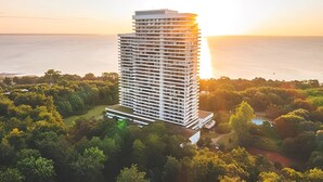 Ein hoch aufragendes Hotel mit modernem Design, umgeben von üppiger Vegetation und Blick auf das Meer bei Sonnenuntergang.
