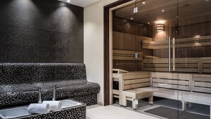 Ein moderner Wellnessbereich mit einer schwarz-weißen Mosaikbank, einer Sauna mit Glasfront und Holzbänken.