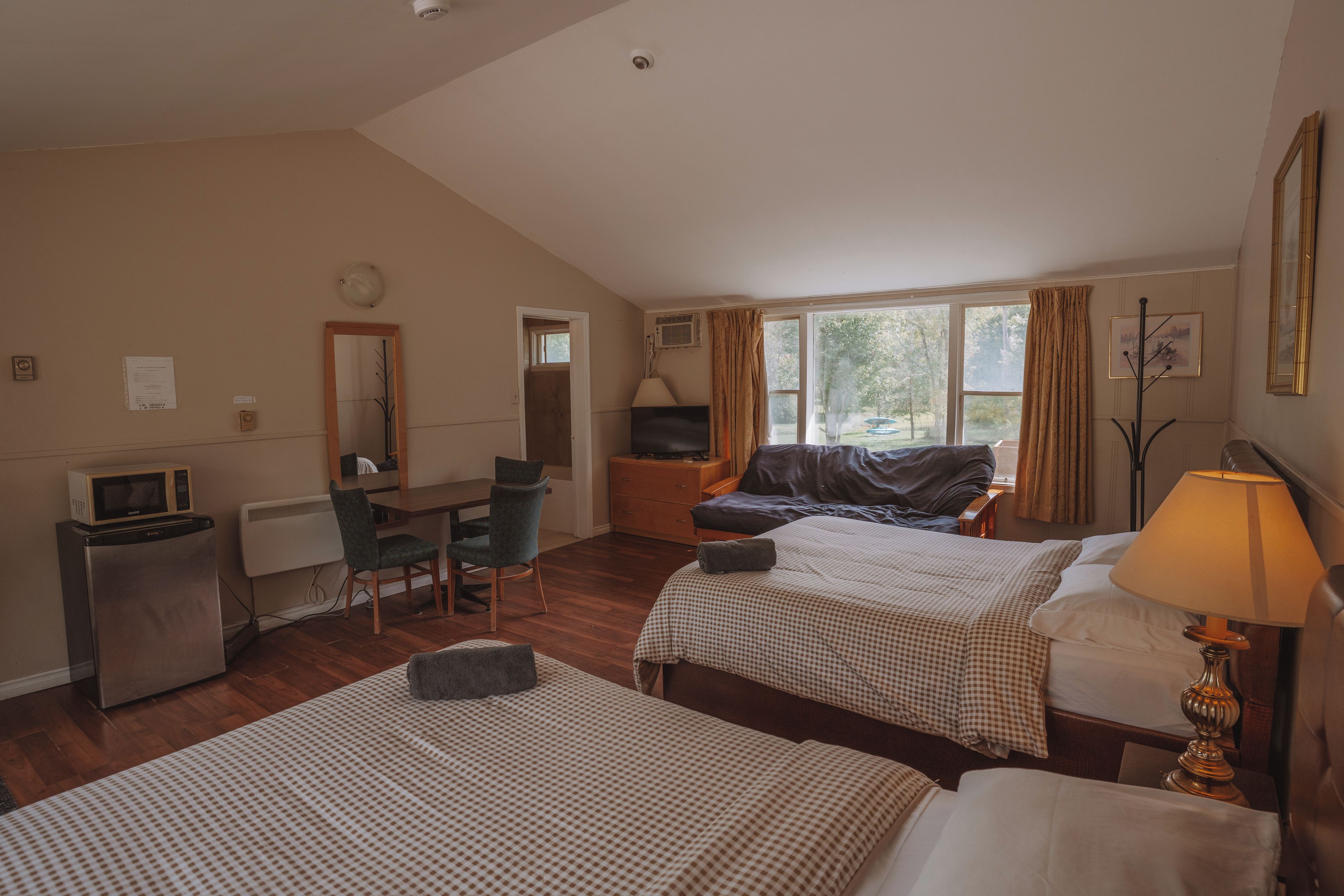 A hotel room with two beds, a desk, a chair, a television, and a window with curtains.
