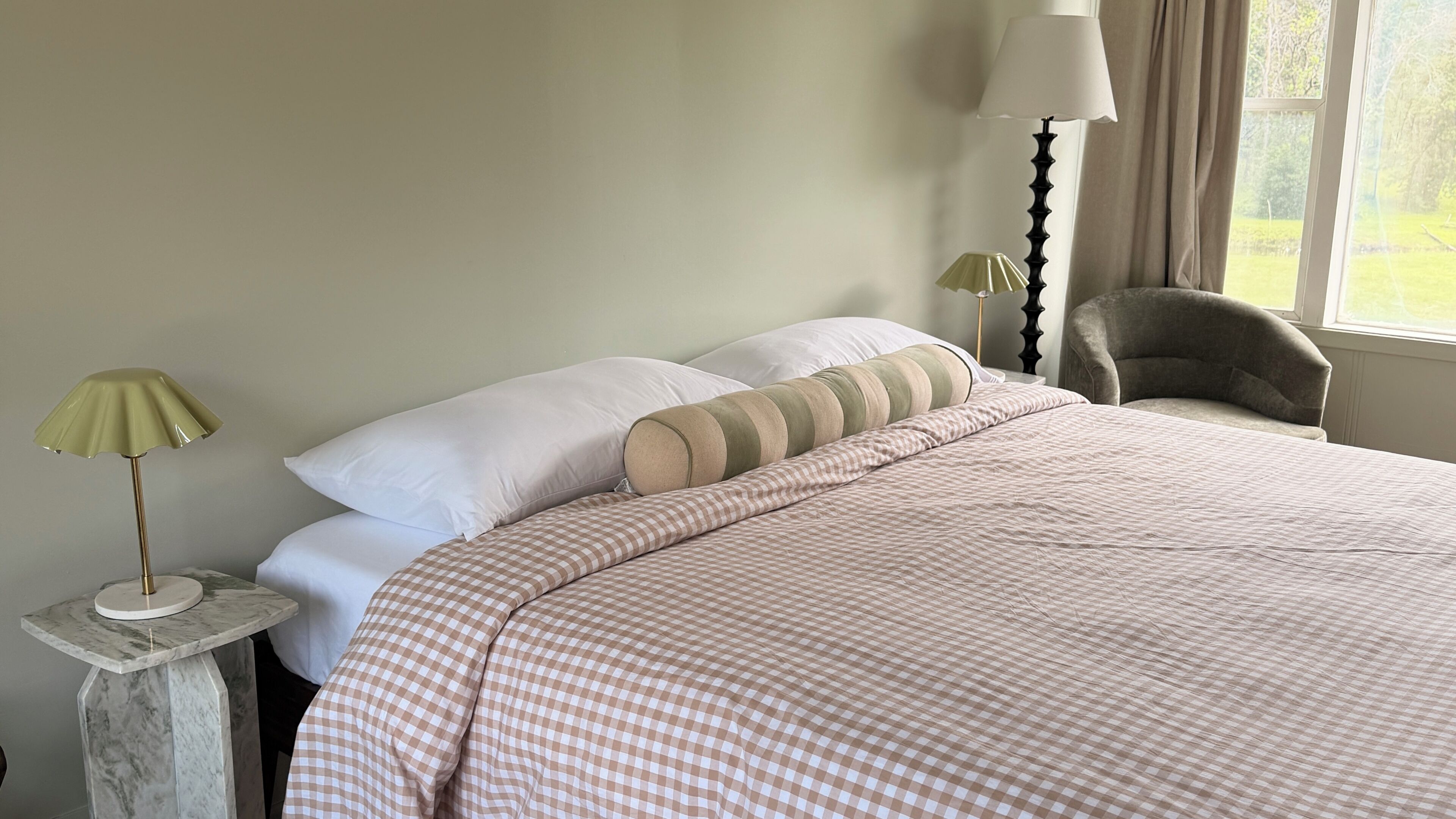 Un dormitorio con cama, almohadas, lámpara y una silla.