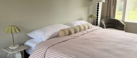 Un dormitorio con cama, almohadas, lámpara y una silla.