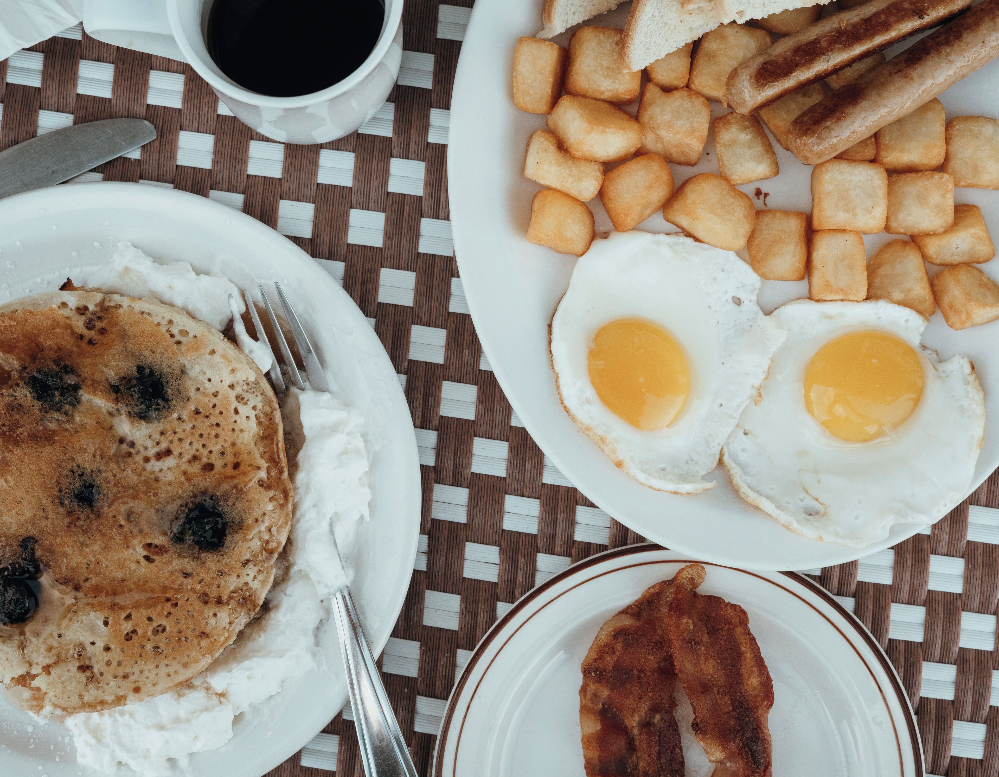 A breakfast plate with pancakes, fried eggs, hash browns, toast, and bacon.