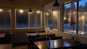L’intérieur d’un restaurant, avec des tables et des chaises en bois, des luminaires suspendus et de grandes fenêtres donnant sur l’extérieur.