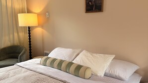 Un lit bien fait, avec une couverture à carreaux, une lampe et un tableau encadré accroché au mur.
